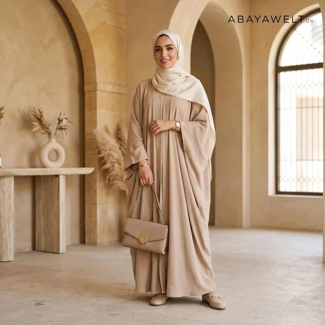 Frau in beiger Abaya mit hellem Hijab und Handtasche in elegantem Interieur