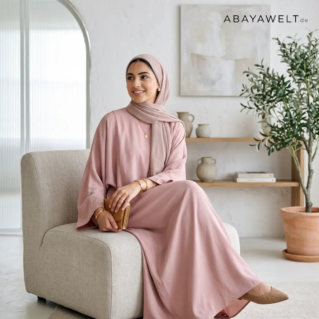 Frau in rosafarbener Abaya mit passendem Hijab in modernem Wohnraum