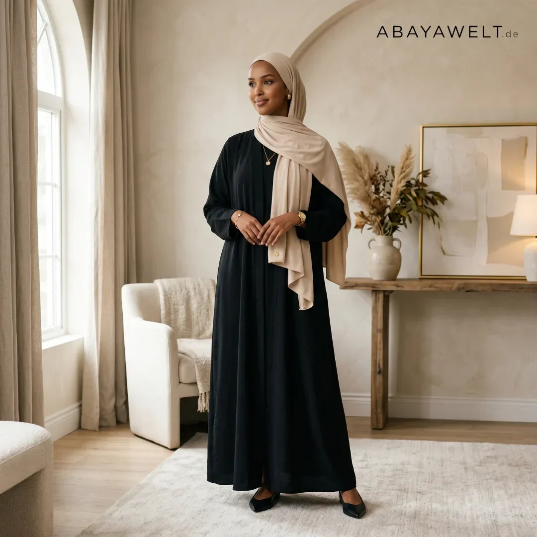 Frau in schwarzer Abaya mit beigem Hijab in einem hellen modernen Interieur
